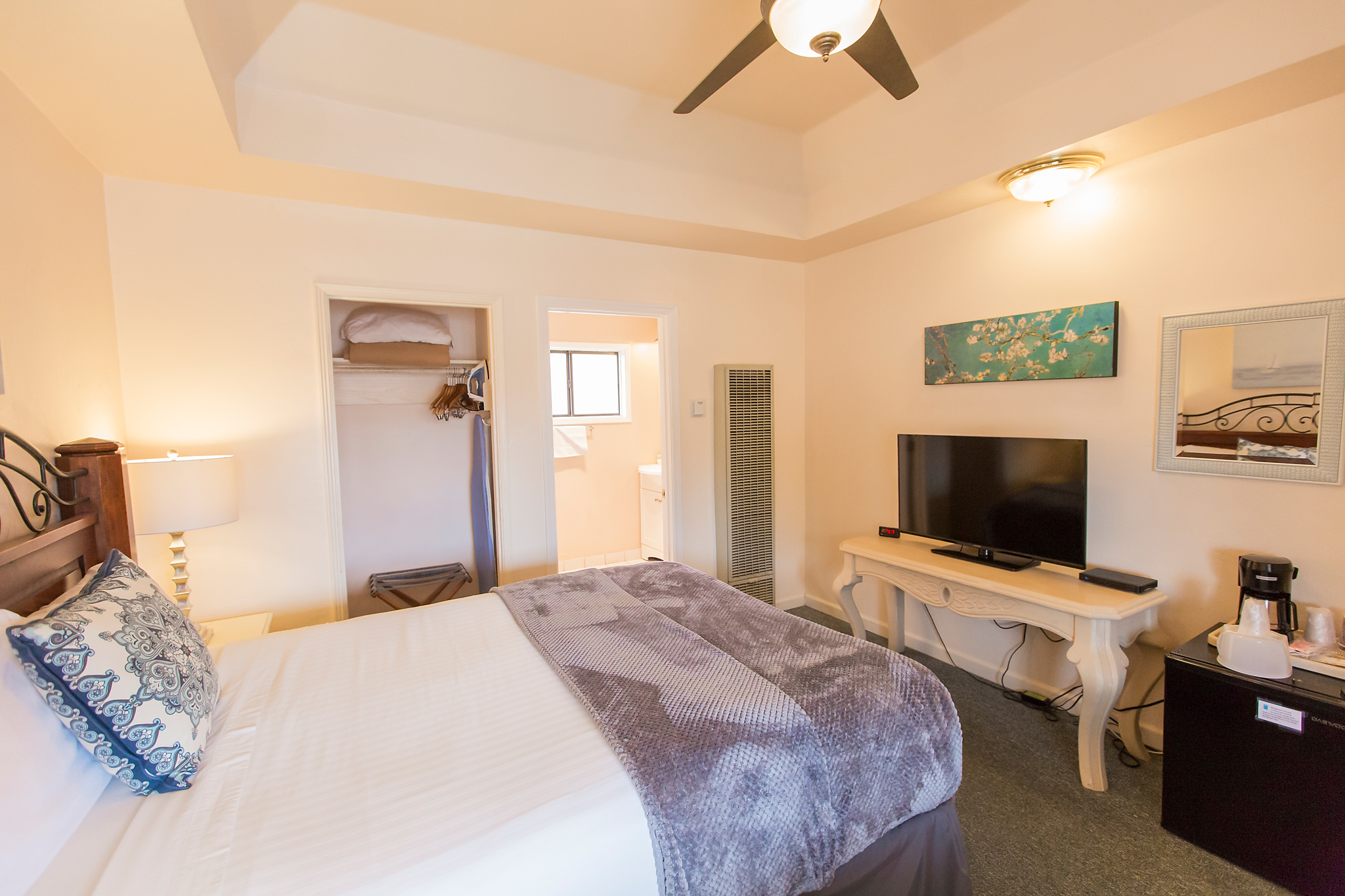 A hotel room with a bed, TV, coffee maker, and closet.