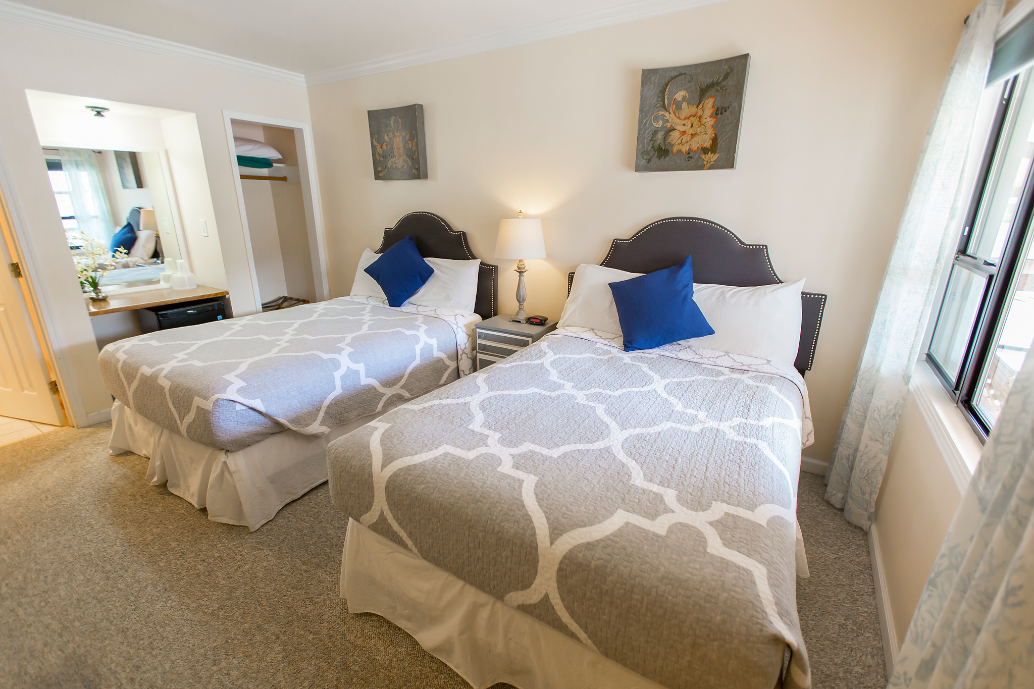 A wide view of a hotel room with two beds, a nightstand, and a window.