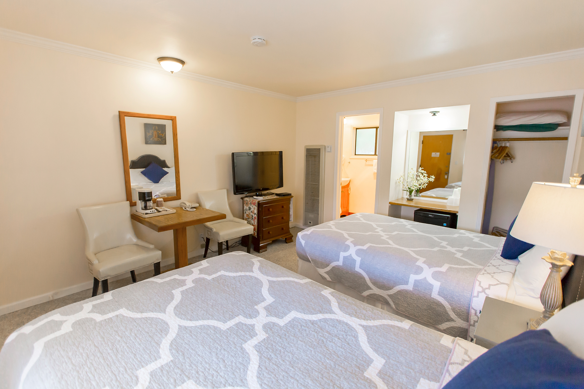 A wide view of a hotel room with two beds, a desk, a TV, and a bathroom doorway.