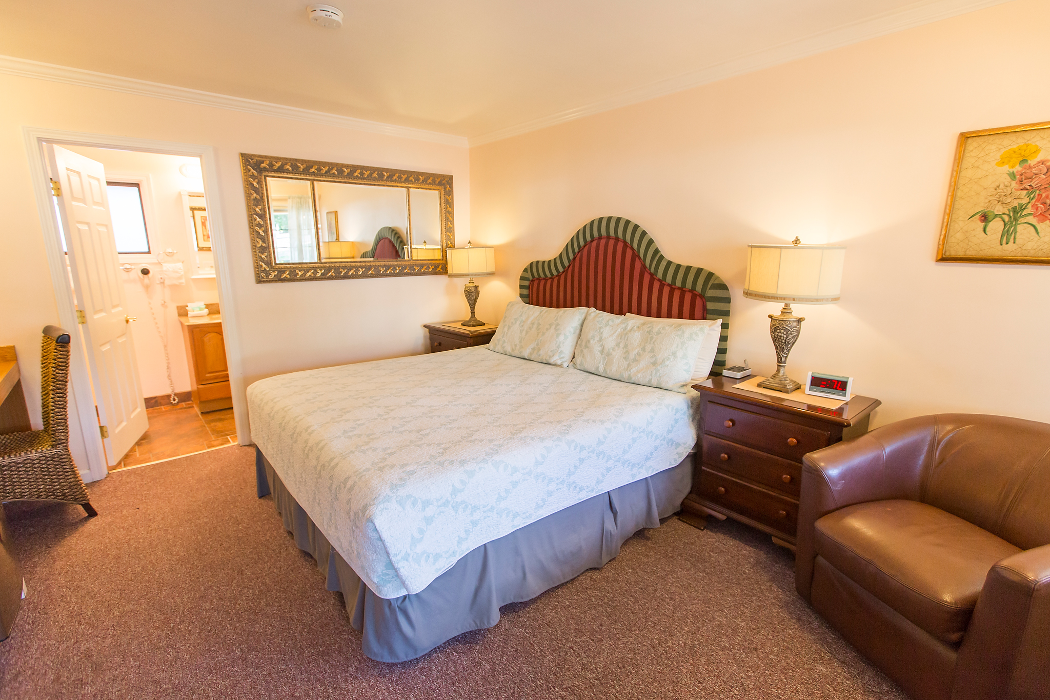 A hotel room with a large bed, wooden nightstand, leather armchair, and open doorway to bathroom