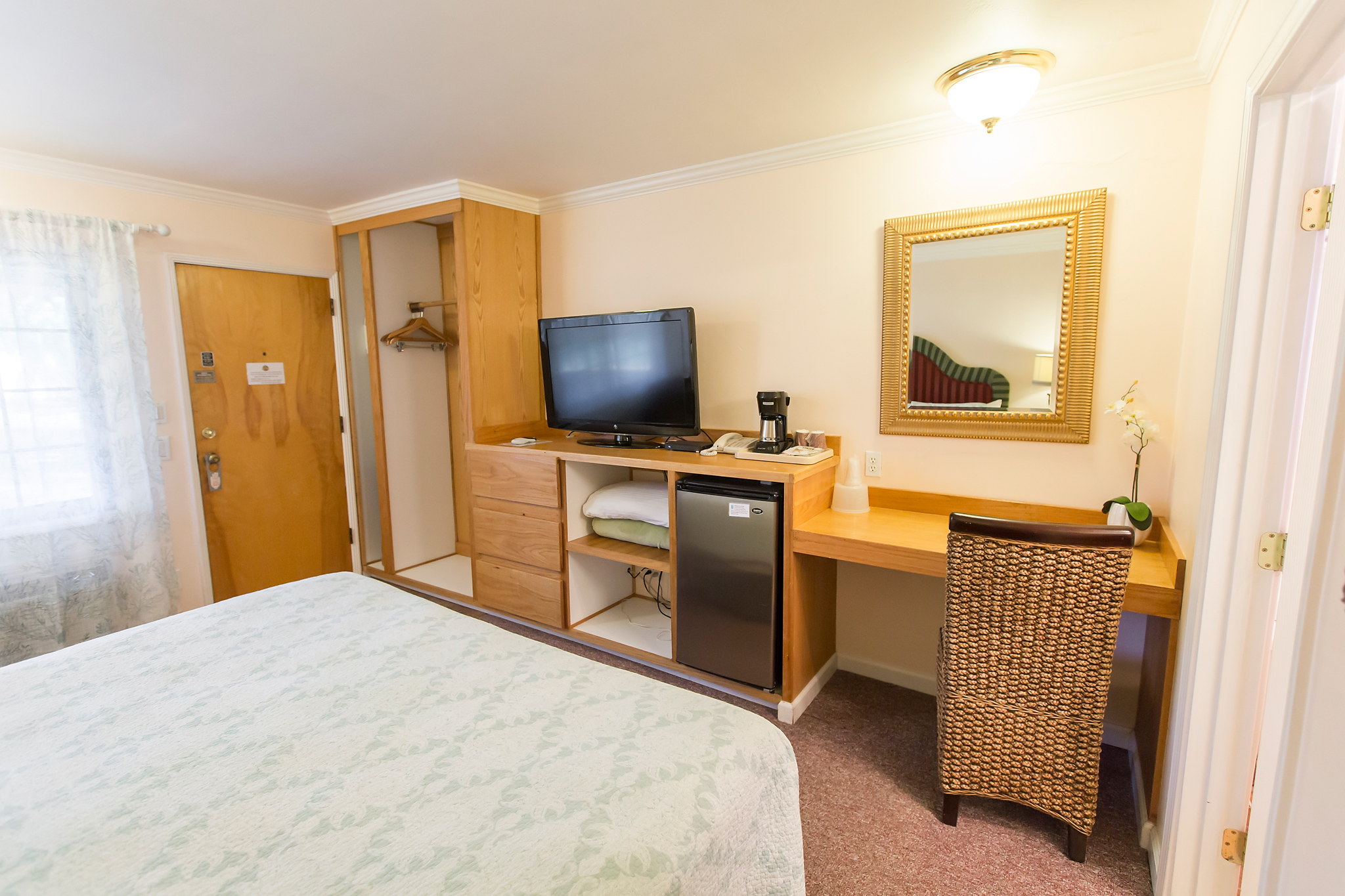 A hotel room with a bed, desk, TV, and mini-fridge.