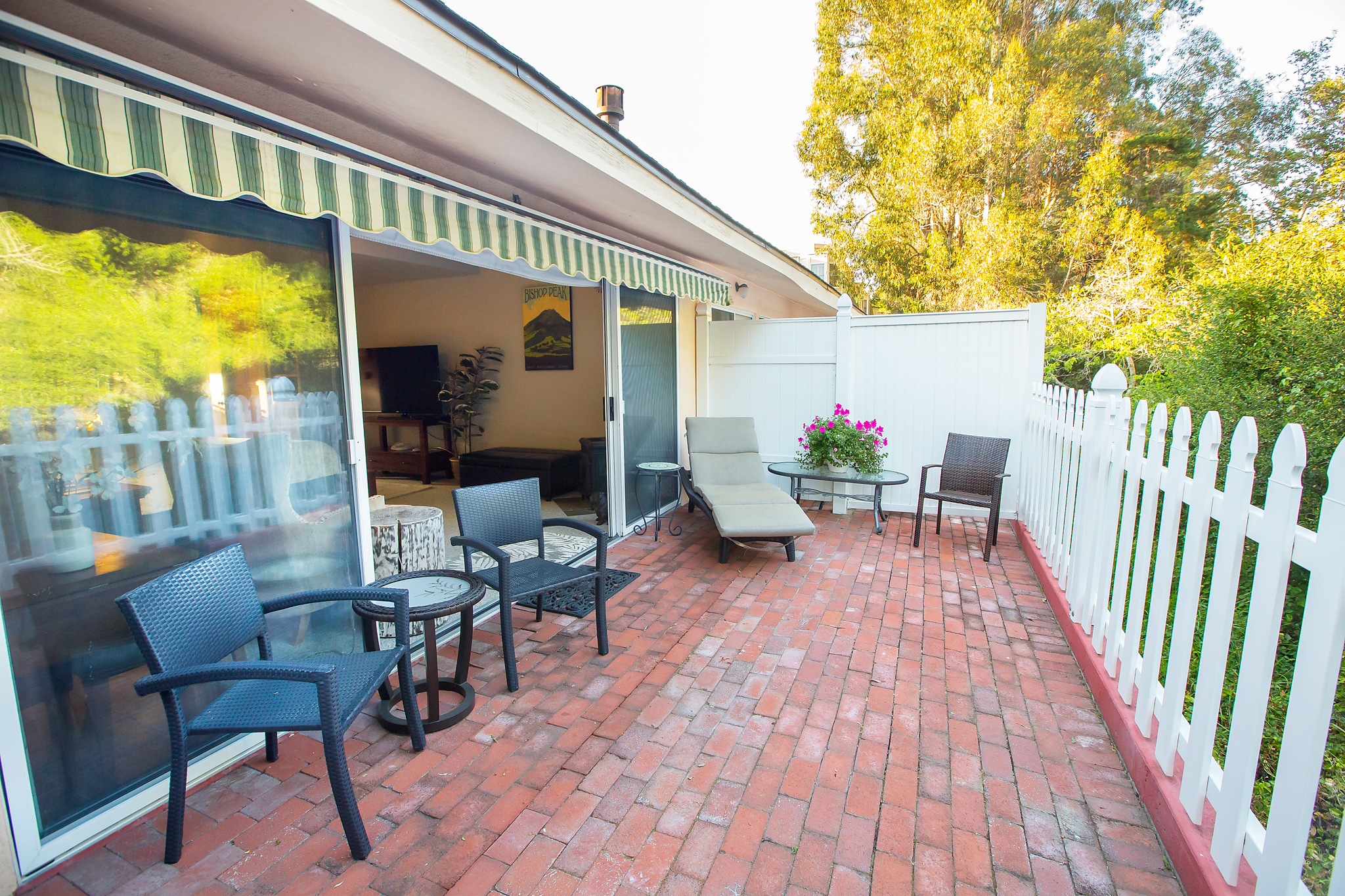 A brick patio with outdoor furniture, a white picket fence, and a green and white awning.